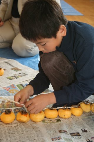 写真:柿を紐に結ぶ寺津小学校児童