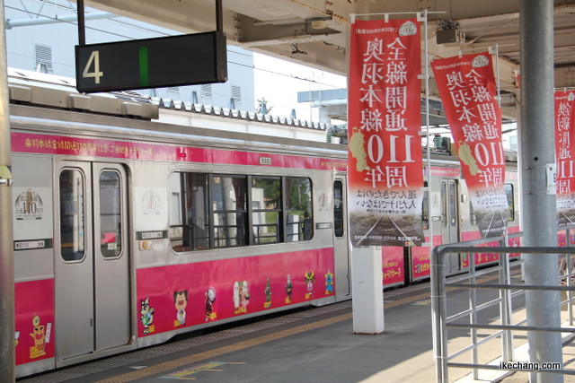 写真：車両とノボリ旗（奥羽本線全線開通110周年記念ラッピング列車ご当地キャラ号）