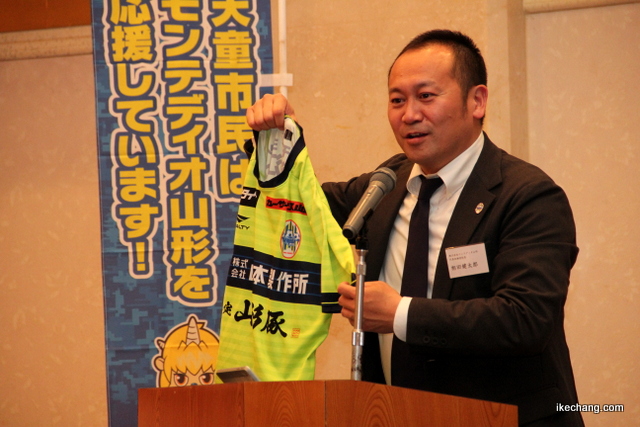 写真：じゃんけん大会の賞品を紹介する相田健太郎社長（天童市モンテ応援隊総会）