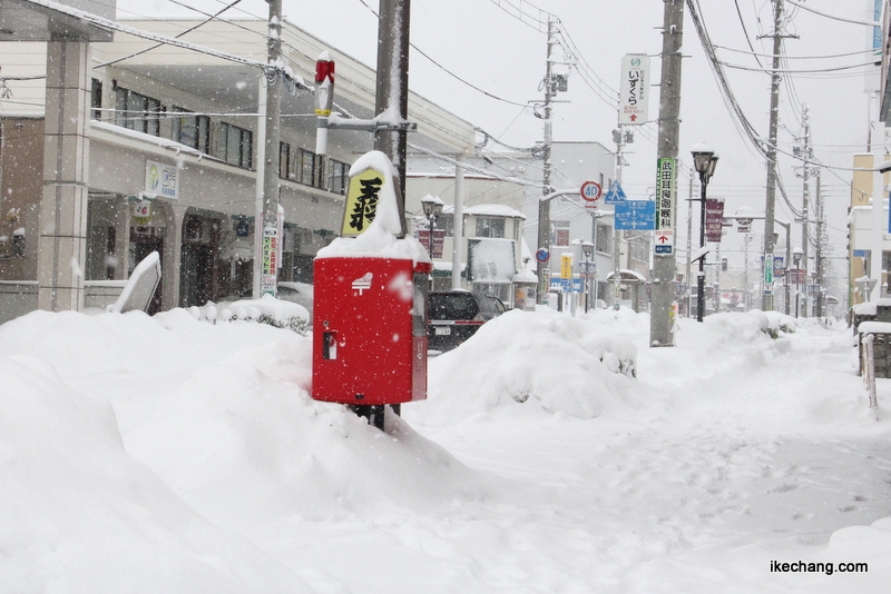 画像：雪で埋まりそうになる将棋駒が乗った郵便ポスト