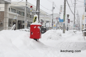 写真：雪で埋まりそうになる将棋駒が乗った郵便ポスト