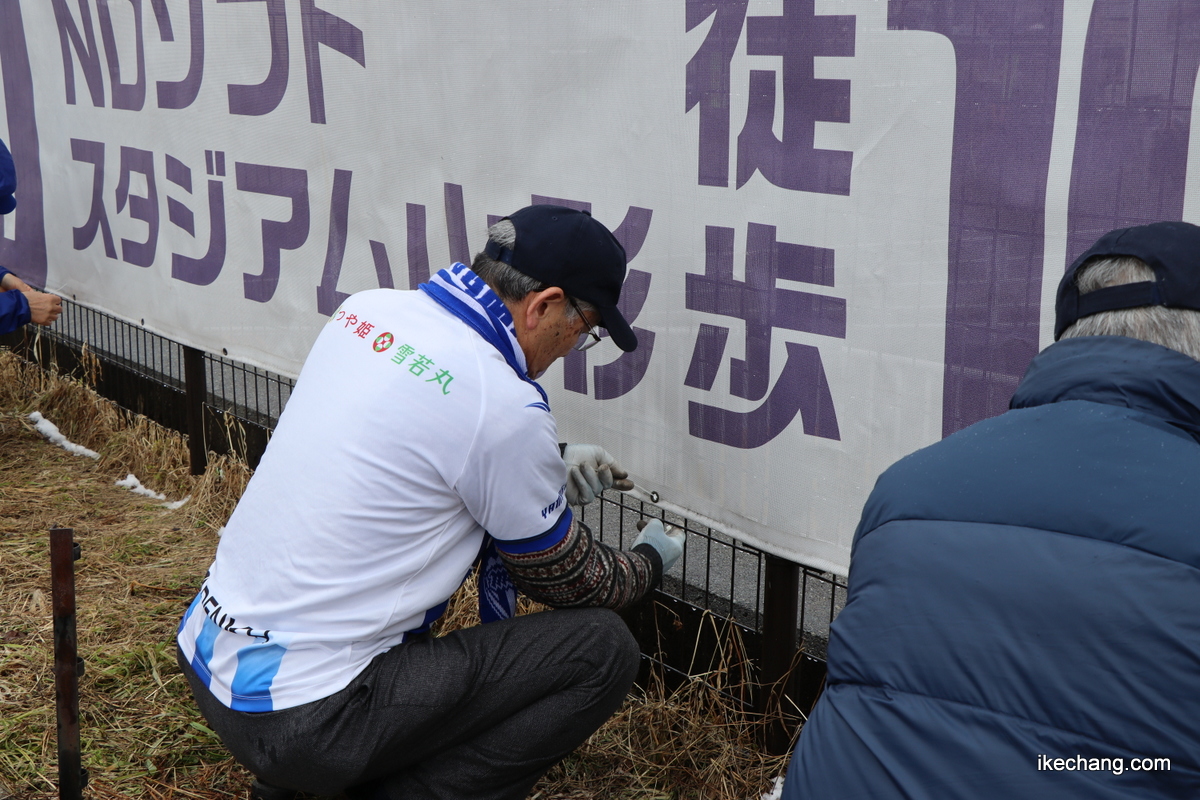 写真：横断幕を結束バンドで固定する天童市モンテ応援隊の参加者